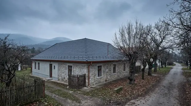 Felújított, sötétszürke tetős kőfalú családi ház ködös őszi időben